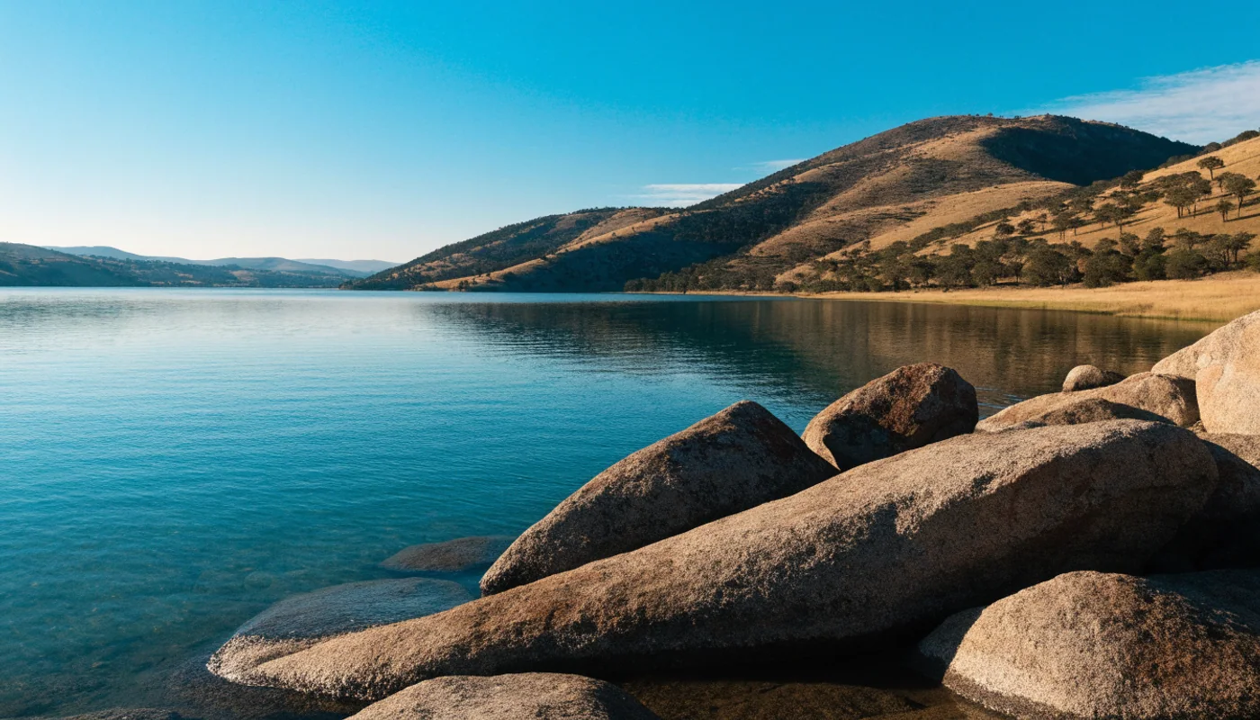 Granite boulders along a reservoir shore with dry foothills in a California scene.
