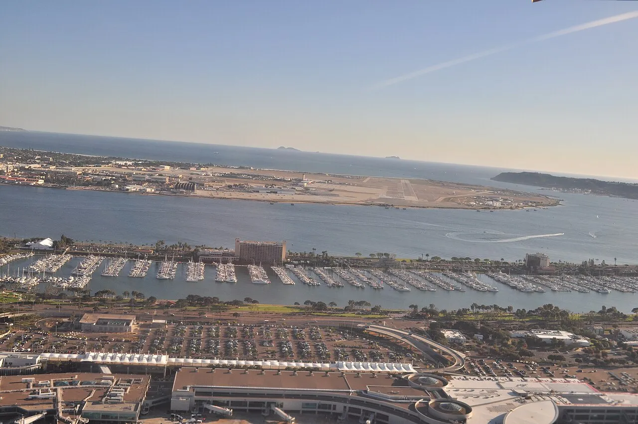 Low aerial from over San Diego International Airport, San Diego, California (terminals partly visible in foreground), looking south across North San Diego Bay to Naval Air Station North Island on Coronado Island. In the middle ground is the Sheraton